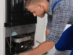 Refrigerator repair technician servicing the compressor and condenser area in Riverside, CA